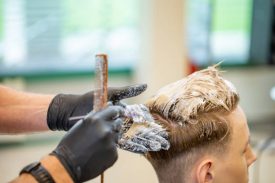 Hairdresser Bleaching Hair of a Young Adult Man.