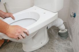 Repairman hands installing flush toilet, toilet bowl in the bathroom